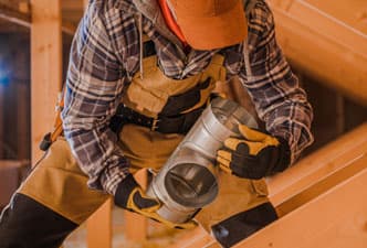 A contractor stands in an attic holding a piece of HVAC ducting